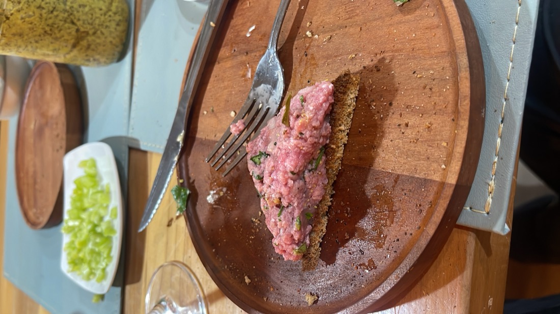 Foto original tomada con el celular: tártaro de res sobre una tabla, en una mesa desordenada de restaurante
